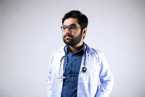 person wearing white coat, stethoscope, and dress shirt with an expression of apathy